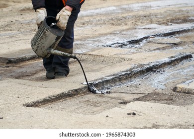 A road worker pours molten bitumen from a watering can onto the milled edges of the pit.                                 - Shutterstock ID 1965874303