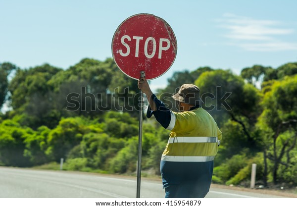 Road worker slows traffic with stop sign. Man\
construction apprentice holding a stop sign and directing traffic\
on the road at Australia.