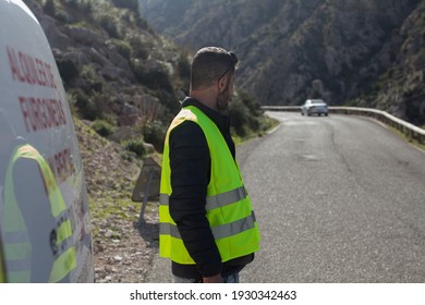 A Road Worker With A Walkie Talkie And A Reflective Vest While Holding A Stop Sign On A Mountain Road In Majorca