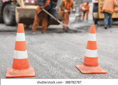 Road Workers Repair The Road,  Cones In  Foreground