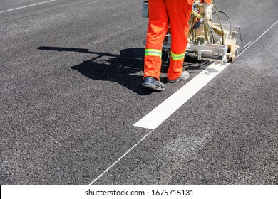 Road workers use hot-melt scribing machines to painting dividing line on asphalt road surface in the city.