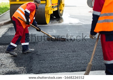 The road workers' working group updates part of the road with fresh hot asphalt and smoothes it for repair.