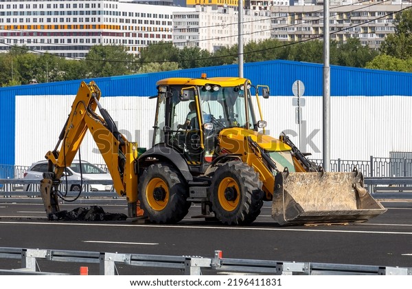 Road works in the city. A yellow wheeled tractor\
breaks asphalt with a jackhammer to install dividing fences between\
road lanes