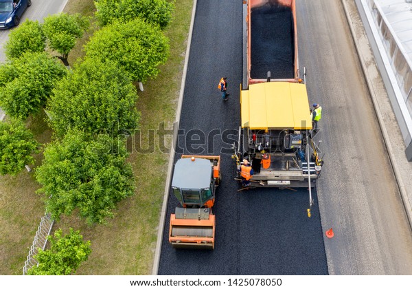 Road works. Laying asphalt in the\
city.  Shown asphalt paver, asphalt rink and dump truck with\
asphalt. Nearby is a team of road workers. The view from the\
top.