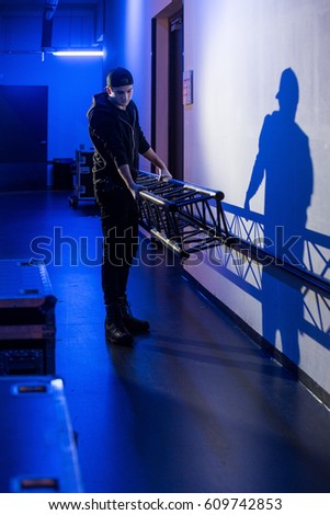 Roadie carrying a big truss support to the stage, casting a shadow on the wall,