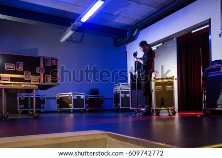 Roadie preparing a microphone on a tripod for the singer, near the stage entrance, prepairing for a concert, surrounded by flight cases.