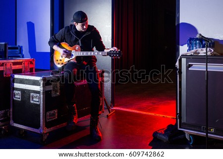 Roadie tuning a guitar for the guitarist next to the stage entrance, sitting on a flight case