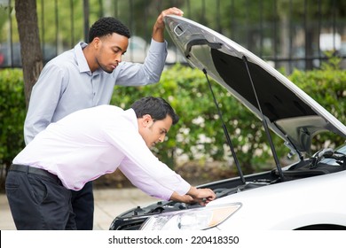Roadside assistance.  Closeup portrait, two frustrated guys trying to figure out how to fix broken down car on side of road, isolated green trees background
