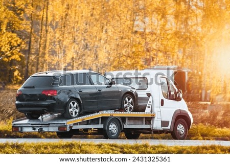 a roadside assistance service on a country road. A tow truck is carrying a car that has been involved in a traffic accident and has a broken engine