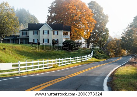 Roadside farmhouse house in countryside rural road highway in West Virginia, USA by mountain forest with colorful autumn fall trees foliage at sunrise morning