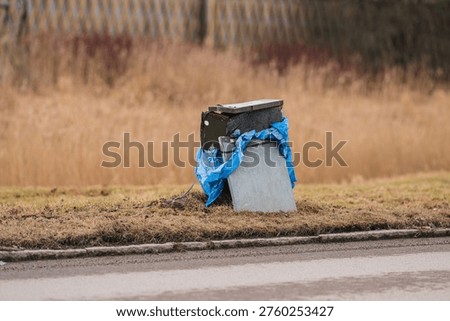 Roadside garbage bin wrapped with blue plastic bag near grassy field