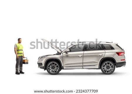 Roadside mechanic holding a tool box and looking at a vehicle with an open hood isolated on white background