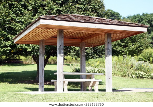 Roadside rest area\
with a picnic table and trees in background. There is a cover or\
canopy over the picnic\
table.