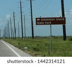 Roadside sign with direction to Galveston Island State Park with rows of power poles in the background