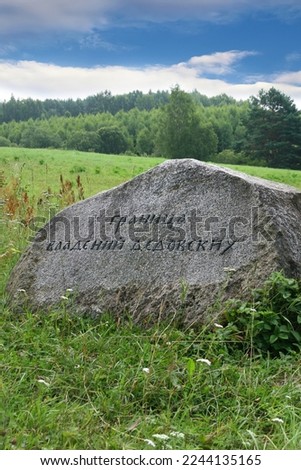 A roadside stone in the grass. Translation of the inscription: The border of the possessions of grandfathers. An ancient stone defining the boundary of the possessions.