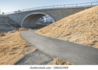 A Roadway Leading Towards A Stone Bridge Next To Dry Grass Hill