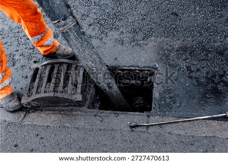 Roadworkers opened clogged road gully and cleaning it from debris and dirt using vac-ex and power jet wash