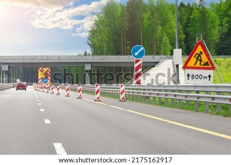 Roadworks, large bright mobile sign with stripes, detour direction and flashing yellow arrow on road service truck trailer in right lane on highway