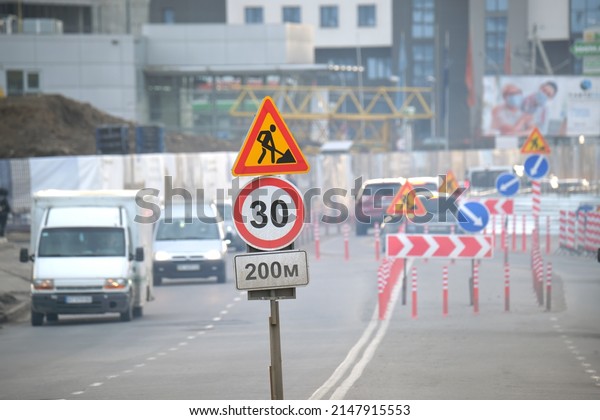Roadworks warning traffic signs of\
construction work on city street and slowly moving\
cars