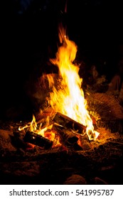 A Roaring Camp Fire Burns At A Camp Site, Nearby Wood Has Been Collected And Stacked In The Pile, Burning For Many Hours In To The Night.