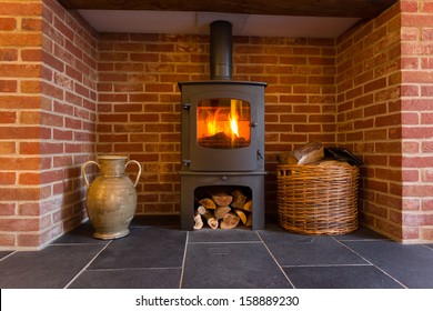 Roaring fire inside wood burning stove in brick fireplace with basket of cut wood ready for burning