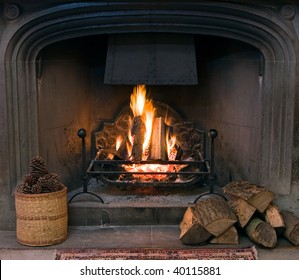 A roaring fire within a large stone arched fireplace, with pile of logs and basket of pine kernels in the foreground.