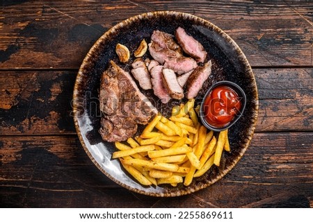 Roast BBQ pork chop steak on plate with potato chips. Wooden background. Top view.