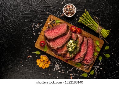 Roast Beef. A Large Piece Of Meat With Fresh Vegetables Is Cut On A Board And Ready To Eat. Black Background. Top View. Close Up And Horizontal Orientation. 
