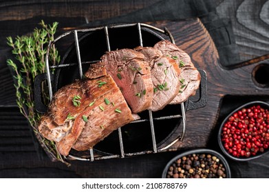 Roast beef on a grill, tenderloin sliced meat with herbs. Black Wooden background. Top view