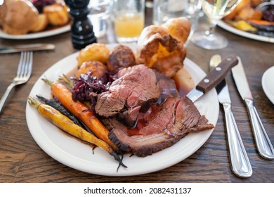 Roast beef on a white plate with roast potatoes and Yorkshire pudding with vegetables in a restaurant.