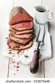 Roast Beef With Sauce And Meat Fork On White Wooden Background