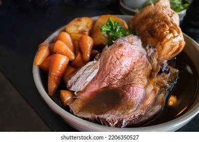 Roast beef slices on a plate with carrots, roast potatoes, a Yorkshire pudding and gravy, making a complete Sunday roast meal. 