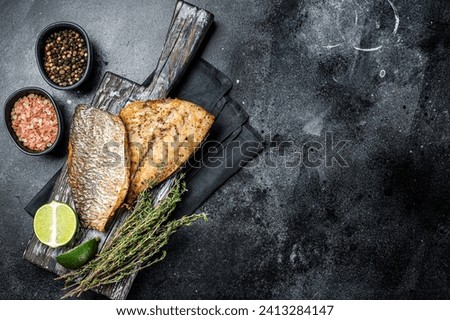 Roast Gilthead Sea Bream fillets with herbs on wooden board. Black background. Top view. Copy space.