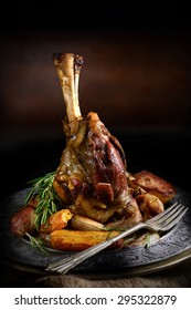 Roast lamb shank with roasted potatoes and carrots styled in a rustic setting with generous copy space. Concept image for home cooking or your bistro or restaurant menu cover design.