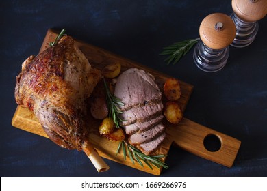 Roast Leg Of Lamb With Potatoes And Rosemary On Serving Wooden Board. View From Above, Top View