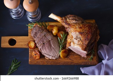 Roast Leg Of Lamb With Potatoes And Rosemary On Serving Wooden Board. View From Above, Top View