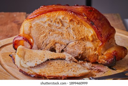 Roast Leg Of Pork Resting On Wooden Chopping Board.