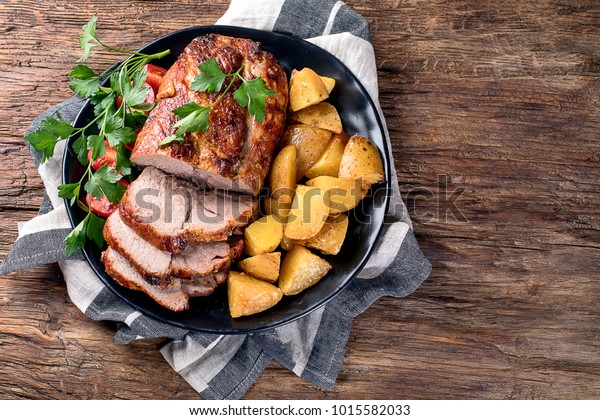Roast pork with herbs and vegetables on rustic\
wooden table.