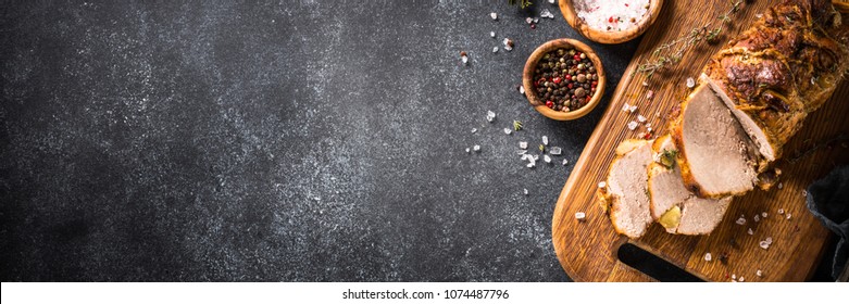 Roast pork meat with herbs and spices on black stone table. Long banner format