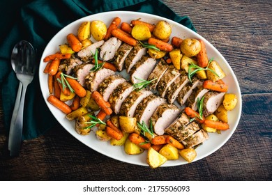 Roast Pork Tenderloin with Potatoes and Baby Carrots: Sliced pork medallions surrounded with vegetables on a platter - Shutterstock ID 2175506093