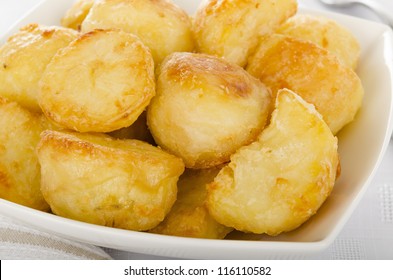 Roast Potatoes - White potatoes roasted with garlic in goose fat in a white bowl. Close  up.