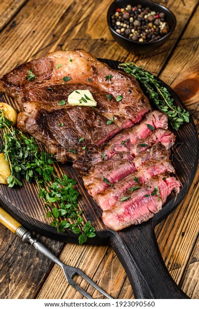 Roast rib eye beef meat steak on a cutting board.\
wooden background. Top\
view