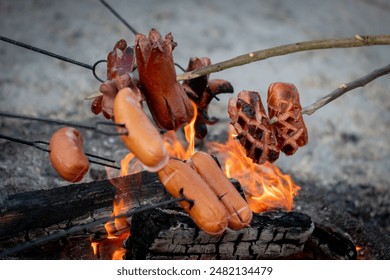 Roast sausage over the fire. Sliced sausages. Sausage impaled on a stick. Fast dinner camping in the countryside. Hot dogs over a small campfire. Grilling sausages over an open fire outdoors. - Powered by Shutterstock