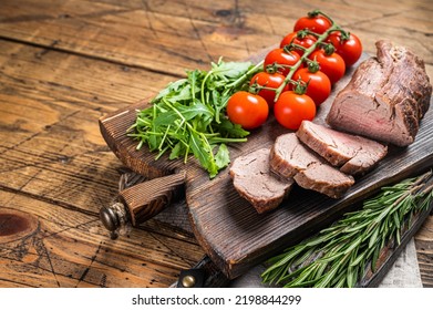 Roast Veal tenderloin, sliced Roastbeef on wooden board with garnish. Wooden background. Top view. Copy space.