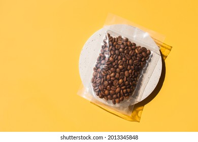 Roasted arabica coffee beans in blank transparent plastic bag with zipper on cement podium and yellow background. Specialty alternative sample trendy concept. Space for text, mock up, top view, flat - Shutterstock ID 2013345848