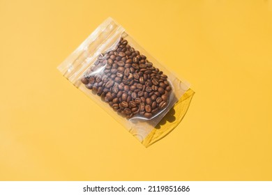 Roasted arabica coffee beans in blank transparent plastic bag with zipper on yellow background. Specialty and alternative sample coffee trendy concept. Mock up, top view, flat lay, isolated - Shutterstock ID 2119851686
