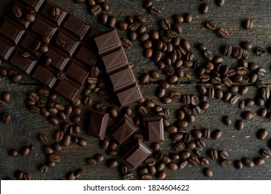 Roasted Arabica Coffee Beans Scattered On A Wooden Table With A Bar Of Dark Chocolate. Fresh Coffee Beans.