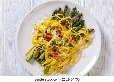 Roasted Asparagus Spears With Spaghetti Sprinkled With Shredded Cheese, Fried Bacon Pieces And Parsley On White Plate On White Textured Wood Table, Flat Lay, Close-up