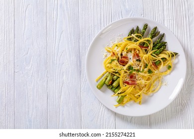 Roasted Asparagus Spears With Spaghetti Sprinkled With Shredded Cheese, Fried Bacon Pieces And Parsley On White Plate On White Textured Wood Table, Flat Lay, Free Space