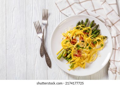 Roasted Asparagus Spears With Spaghetti Sprinkled With Shredded Cheese, Fried Bacon Pieces And Parsley On White Plate On White Textured Wood Tablewith Forks, Flat Lay